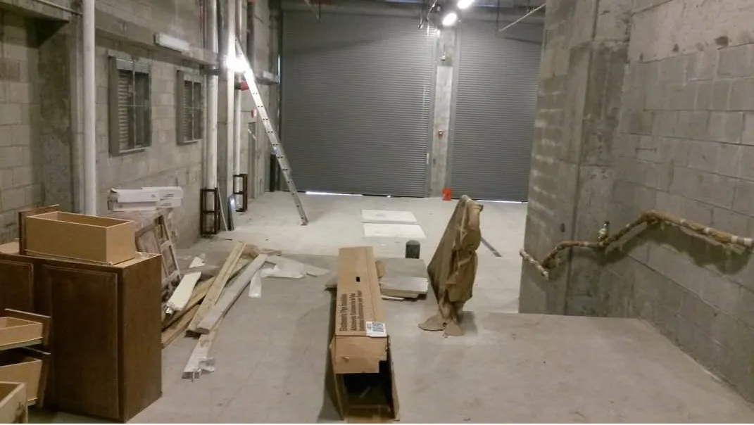A real Faithful Cleaning Service construction site - a commercial interior with leftover lumber, cardboard and materials on a bare concrete floor, before the post-construction clean