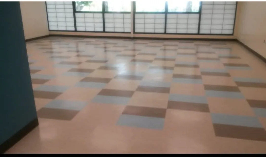 A large commercial room with a multi-color vinyl tile floor that has been stripped and waxed to an even reflective shine, with daylight from a wall of windows