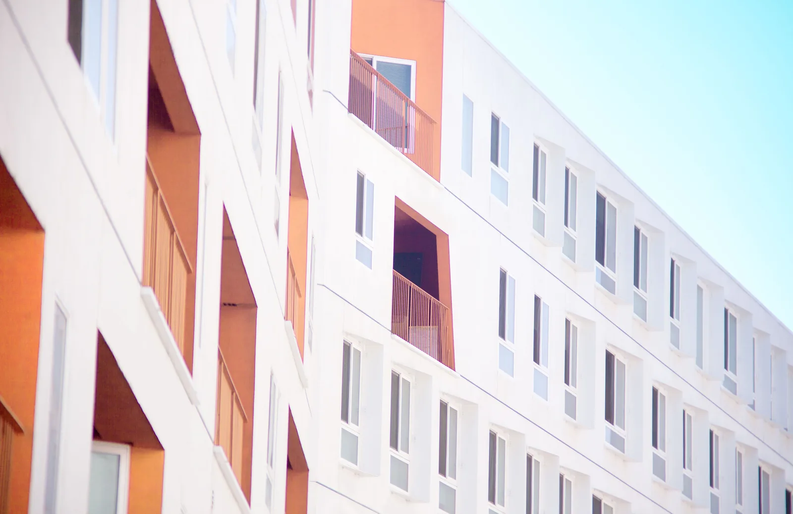 The exterior of a newly finished multi-story residential building with white and orange facade panels and balcony railings