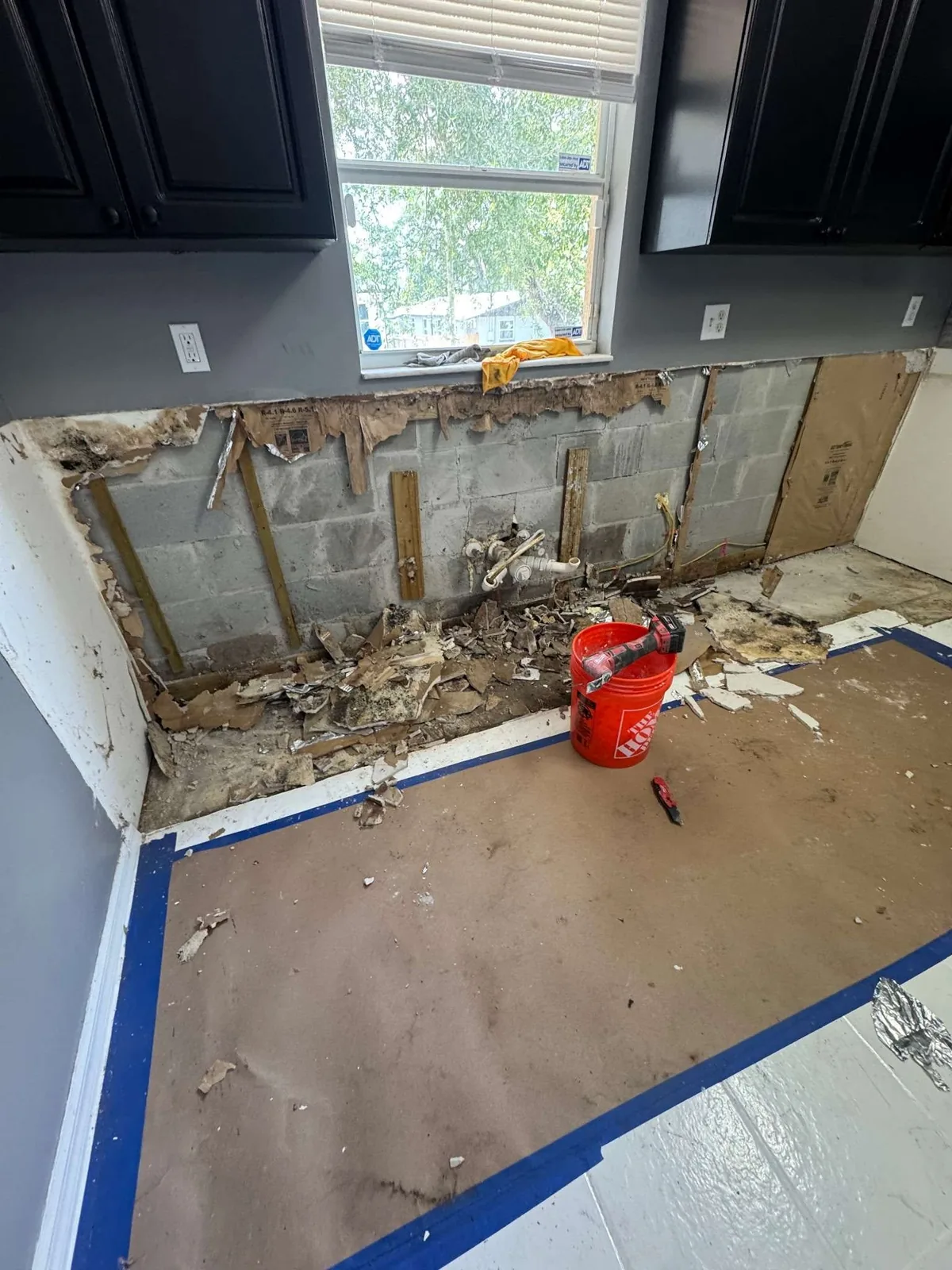 A gutted kitchen wall during demolition with the block exposed and debris cleared after water damage was found