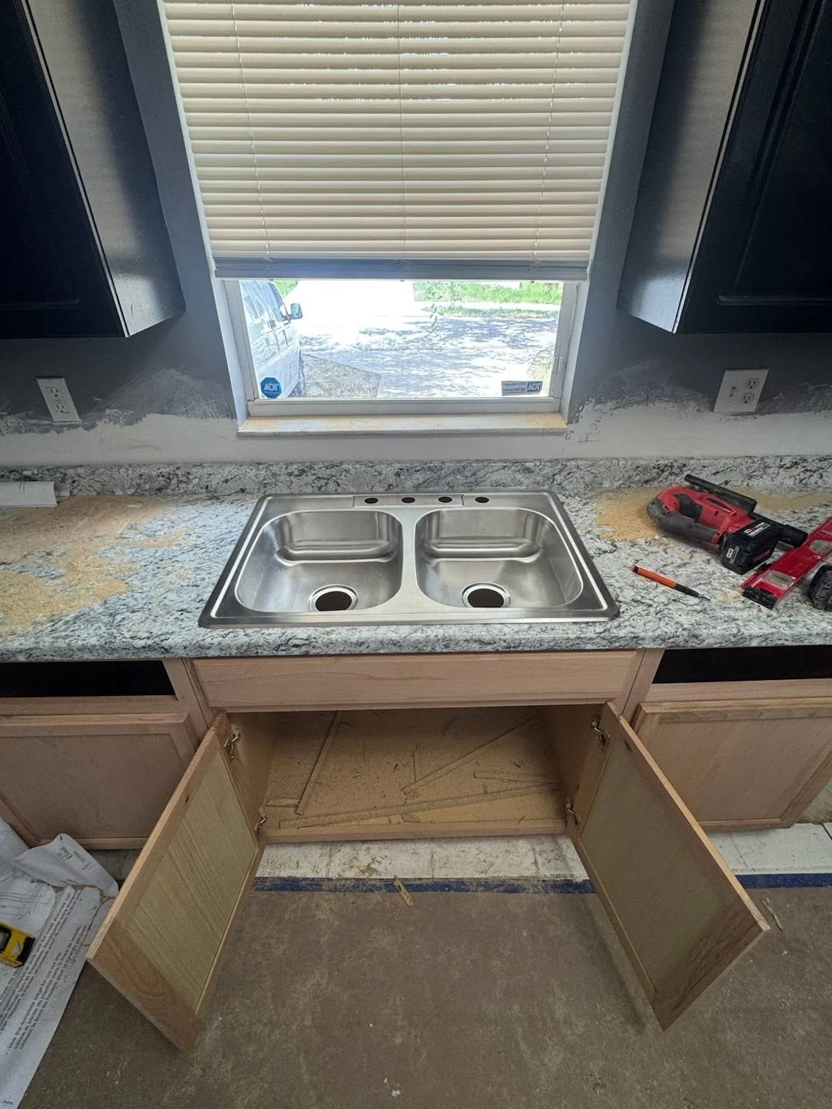 A new stainless steel sink being set into the fresh granite countertop during the rehab