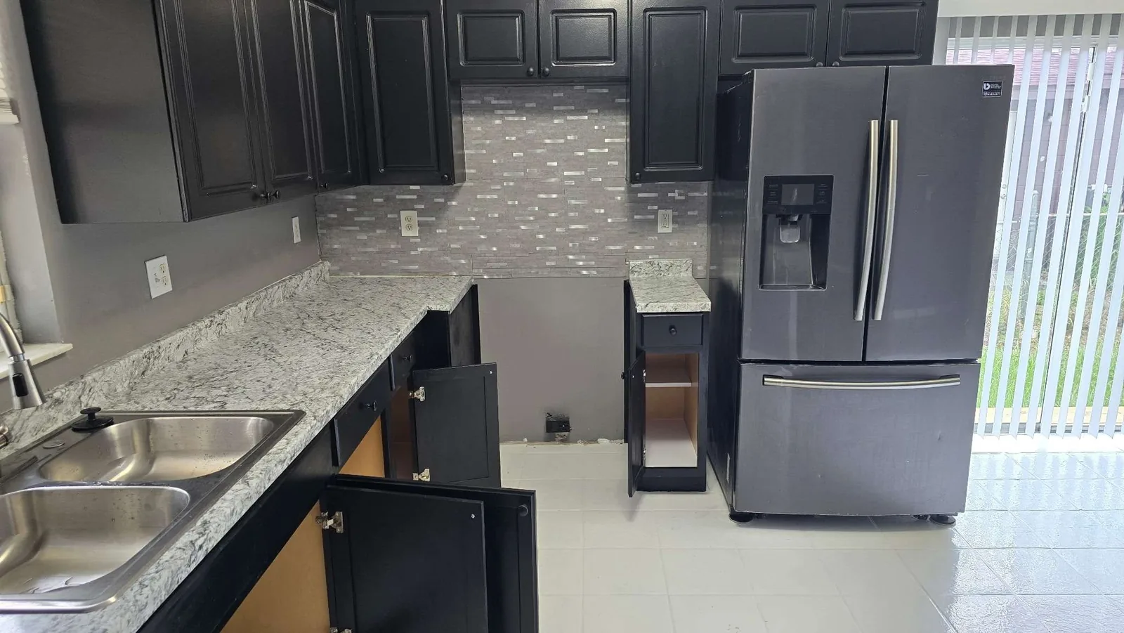 The finished kitchen wall run with repainted black cabinets, a new granite countertop and a tile backsplash after the rehabilitation